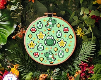 May include: A cross-stitch embroidery hoop featuring a green Yoshi design with stars, eggs, and mushrooms on a light green background. The hoop is set against a backdrop of lush greenery and flowers, creating a vibrant and colorful display.