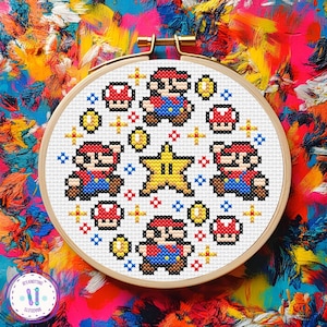Può includere: Un telaio da ricamo a punto croce con un disegno pixelato del personaggio del videogioco Mario, insieme a funghi, monete e una stella. Il disegno è in rosso, blu, giallo e nero. Il telaio è posto su uno sfondo astratto colorato.