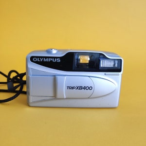 May include: A silver Olympus Trip XB400 film camera with a black lens and a black strap.
