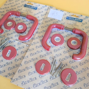 May include: Red door handles, keyhole covers, and hardware are displayed on printed packaging. The handles have a curved design. The keyhole covers are round. The hardware includes small silver nails. The packaging has text in a foreign language.