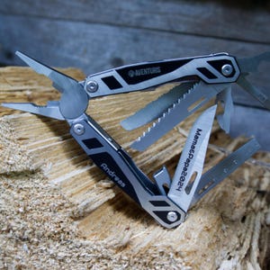 Könnte beinhalten: Ein silbernes und schwarzes Multitool mit einem schwarzen Griff und den eingravierten Worten "Aventuris" und "Andreas Mama's Papa 2024". Das Multitool ist geöffnet und es sind eine Säge, eine Messerklinge und eine Zange sichtbar.