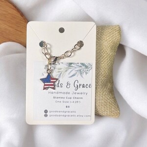 May include: A gold chain bracelet with a star-shaped charm featuring the American flag. The charm is attached to the chain with a gold jump ring. The bracelet is displayed on a white card with the text "ds & Grace Handmade Jewelry Stanley Cup Charm One Size (-4.25) $8 goodsandgracelic goodsanagracelic etsy com".