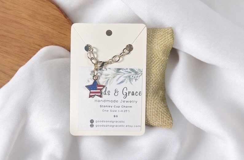 May include: A gold chain bracelet with a star-shaped charm featuring the American flag. The charm is attached to the chain with a gold jump ring. The bracelet is displayed on a white card with the text "ds & Grace Handmade Jewelry Stanley Cup Charm One Size (-4.25) $8 goodsandgracelic goodsanagracelic etsy com".