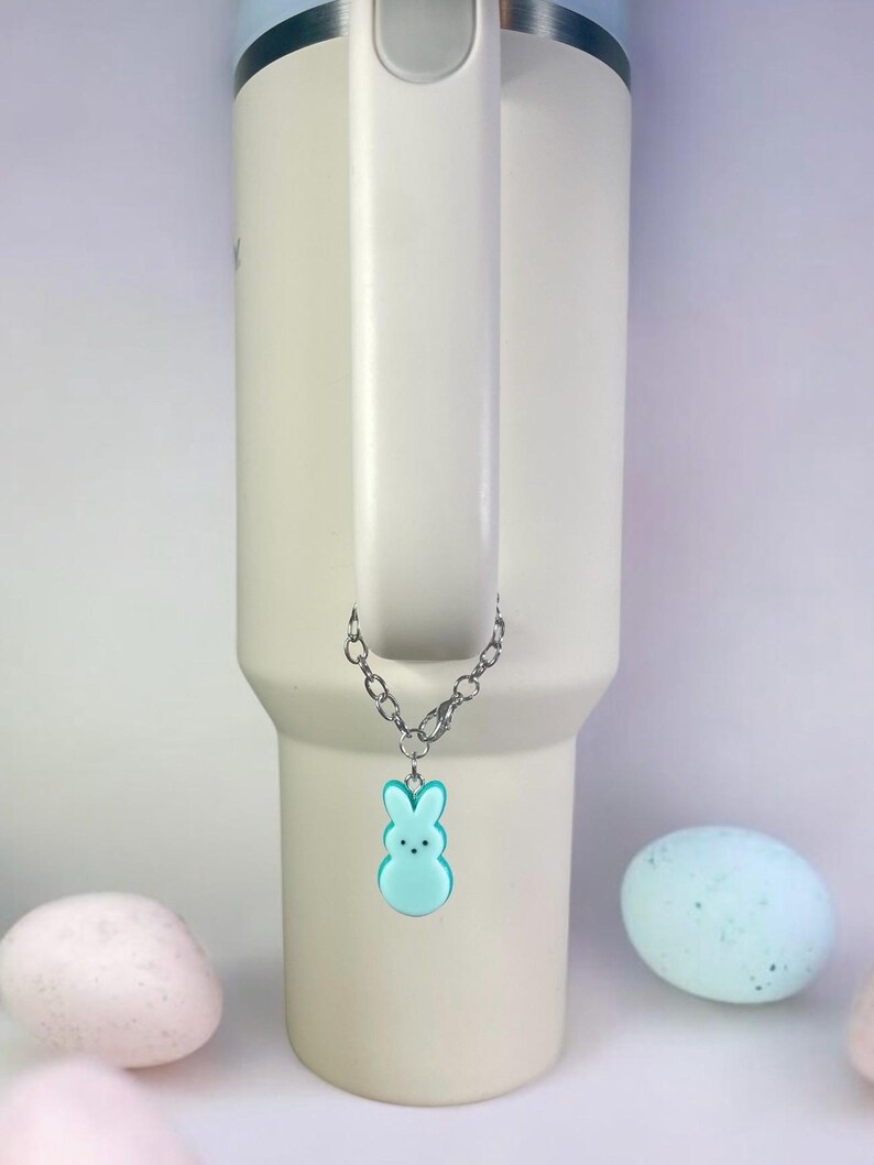 May include: A light blue bunny charm hangs from a silver chain attached to a white travel mug. The mug has a blue lid and a handle. The charm is a popular Easter candy.
