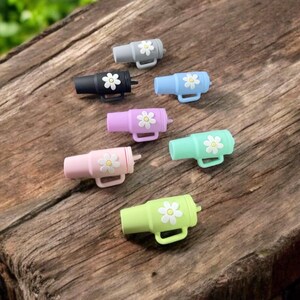 May include: Set of six colorful silicone bottle stoppers with a daisy design. Each stopper features a different color and a white daisy with a yellow center.