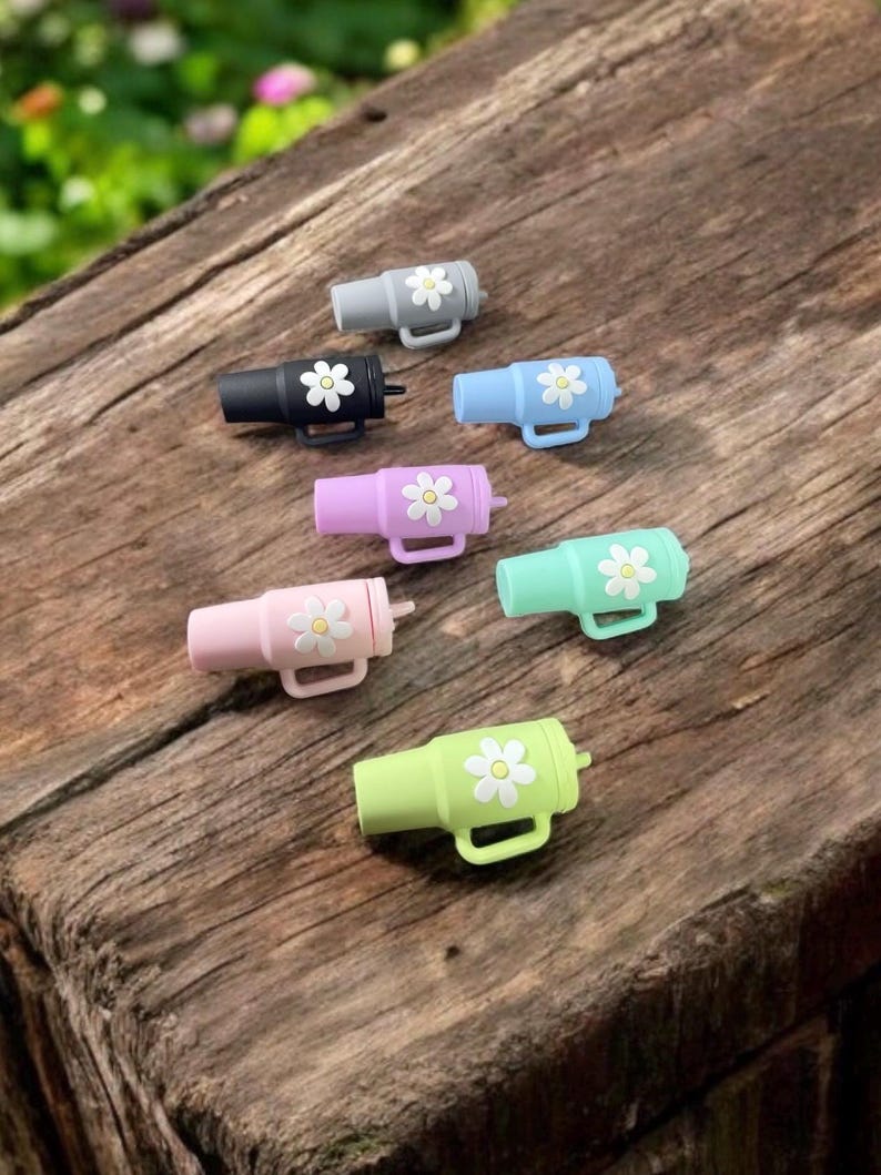 May include: Set of six colorful silicone bottle stoppers with a daisy design. Each stopper features a different color and a white daisy with a yellow center.