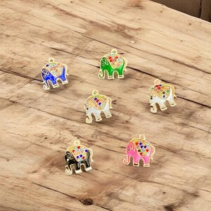 May include: Six colorful elephant charms with gold-colored trim. The elephants are in various colors, including blue, green, white, black, and pink. Each charm has a decorative pattern on its back and a loop at the top for attaching to jewelry or other crafts.