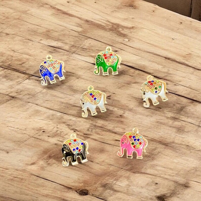 May include: Six colorful elephant charms with gold-colored trim. The elephants are in various colors, including blue, green, white, black, and pink. Each charm has a decorative pattern on its back and a loop at the top for attaching to jewelry or other crafts.