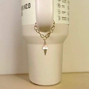 May include: A gold chain with a pink and white ice cream cone charm attached to a white tumbler.