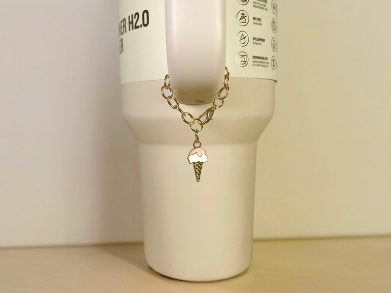 May include: A gold chain with a pink and white ice cream cone charm attached to a white tumbler.