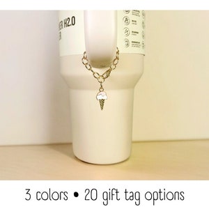 May include: A gold chain with an ice cream cone charm attached to a white tumbler. The tumbler has the text "WATER H2.0" on the side.