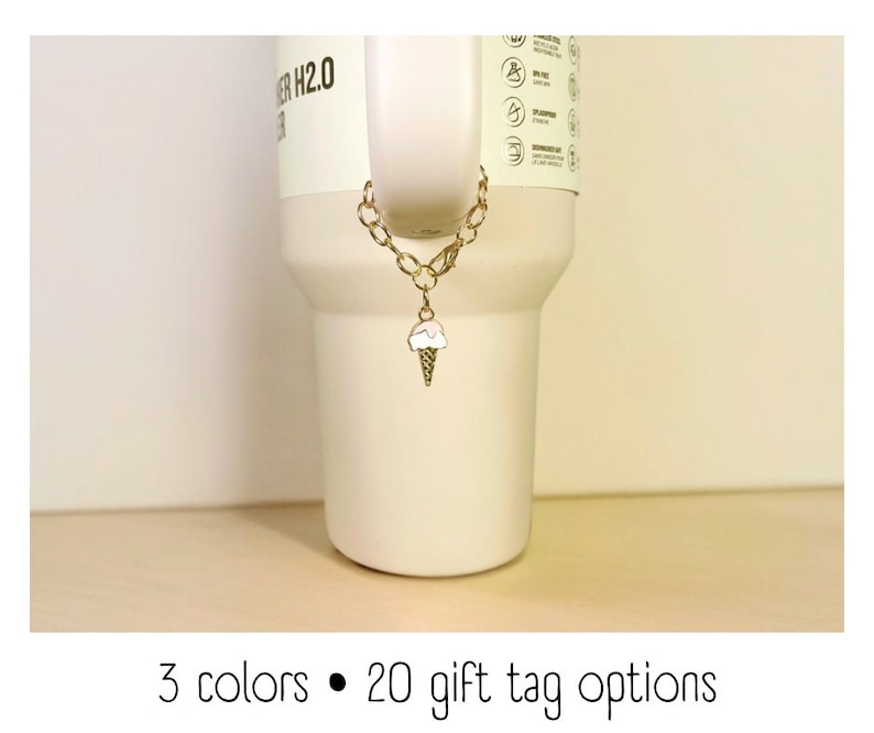 May include: A gold chain with an ice cream cone charm attached to a white tumbler. The tumbler has the text "WATER H2.0" on the side.