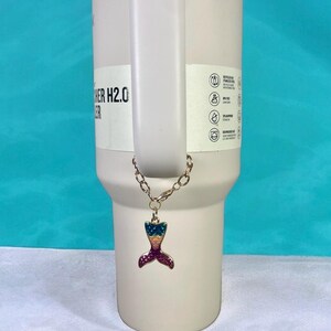 May include: A gold chain with a colorful mermaid tail charm attached to a white tumbler with the text "Other H2.0" on the side.