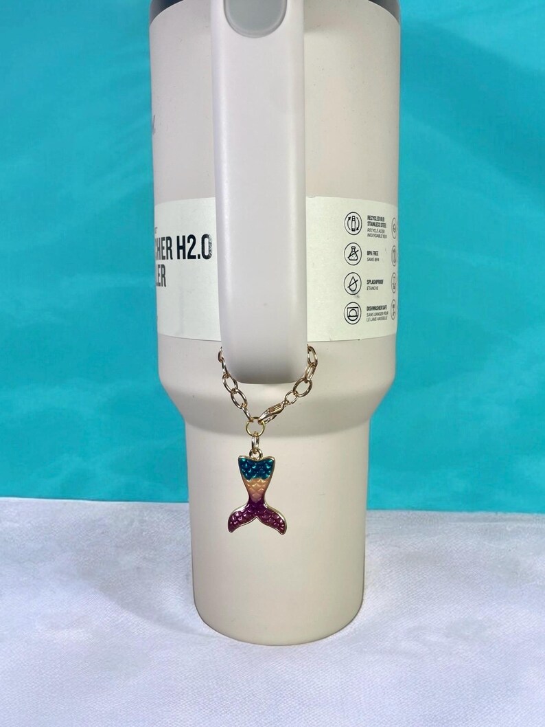 May include: A gold chain with a colorful mermaid tail charm attached to a white tumbler with the text "Other H2.0" on the side.