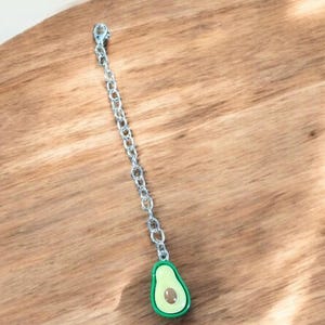 May include: A silver chain with a green avocado charm. The avocado is cut in half and shows the pit inside.