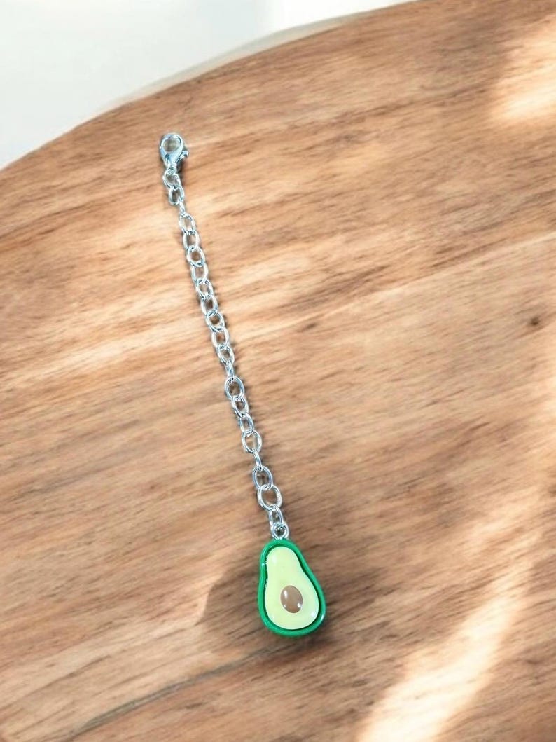 May include: A silver chain with a green avocado charm. The avocado is cut in half and shows the pit inside.