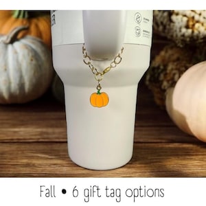 Könnte beinhalten: Ein weißer Becher mit einer goldenen Kette und einem kleinen Kürbis-Anhänger. Der Becher ist von Kürbissen umgeben. Herbst • 6 Geschenk-Etiketten-Optionen.