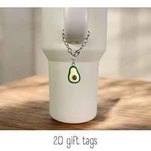 May include: A silver chain with a green avocado charm attached to a white mug. The mug is sitting on a wooden surface. 20 gift tags.