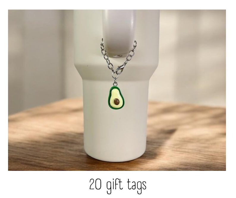 May include: A silver chain with a green avocado charm attached to a white mug. The mug is sitting on a wooden surface. 20 gift tags.