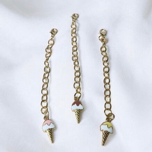 May include: Three gold chains with ice cream cone charms. The charms are different colours: pink, brown, and yellow.