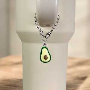 May include: A silver chain with a green and yellow avocado charm attached. The charm is hanging from a white tumbler.