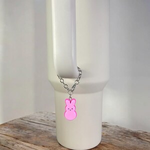 May include: A white travel mug with a pink bunny charm attached to the handle. The charm is on a silver chain.