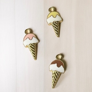 May include: Three gold-coloured ice cream cone charms with different coloured ice cream scoops. The ice cream scoops are yellow, pink, and brown.