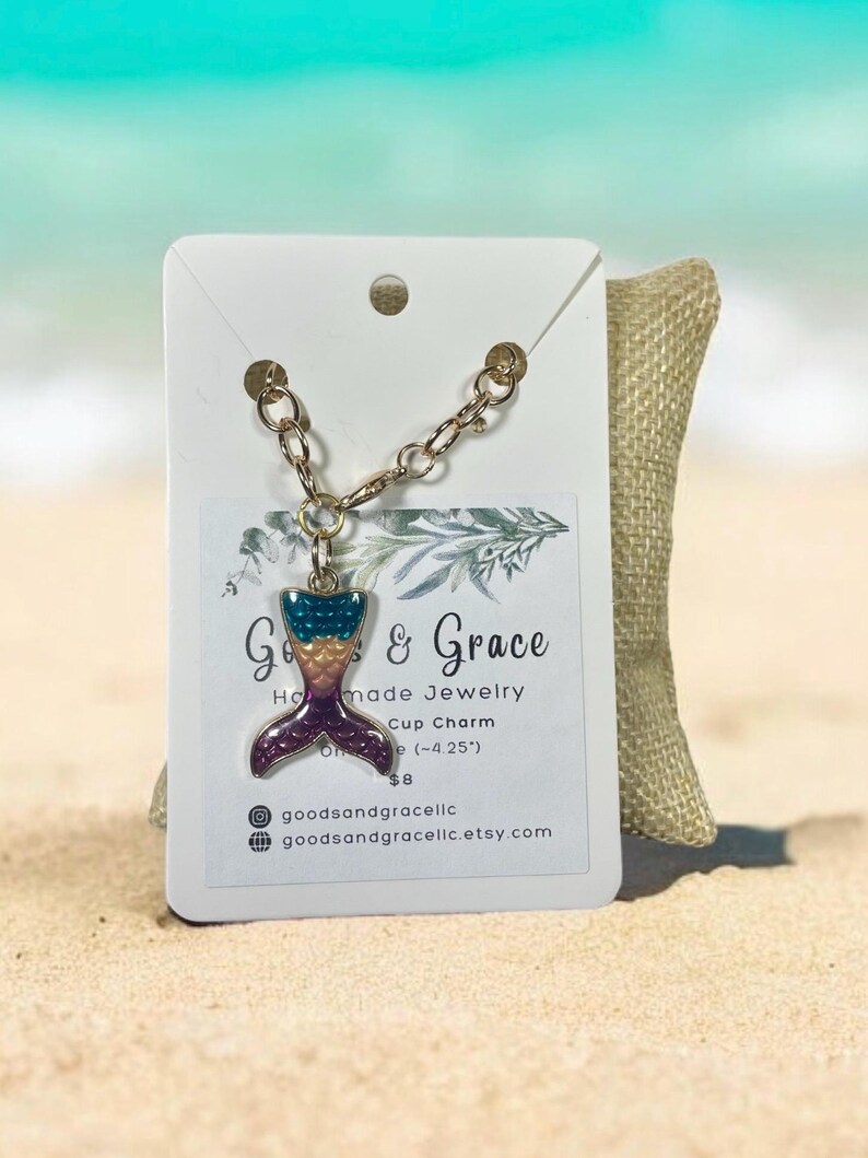 May include: A gold chain with a mermaid tail charm. The charm is purple, teal, and yellow with glitter accents. The charm is 4.25 inches long. The chain is 8 dollars.