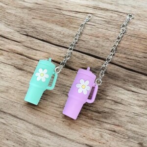 May include: Two small, colorful, plastic bottle stoppers with a daisy design. Each stopper is attached to a silver chain.