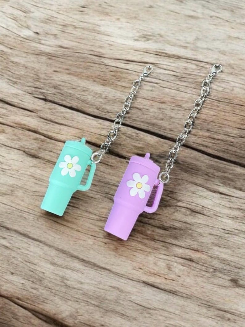 May include: Two small, colorful, plastic bottle stoppers with a daisy design. Each stopper is attached to a silver chain.