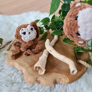 May include: Two brown crocheted monkey toys on a wooden surface with a green plant and driftwood.