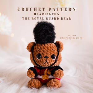 Könnte beinhalten: Ein gehäkelter brauner Bär mit schwarzem Hut und roter und schwarzer Uniform. Der Bär hat große schwarze Augen und einen schwarzen Riemen um sein Gesicht. Der Text auf dem Bild lautet "CROCHET PATTERN BEARRINGTON THE ROYAL GUARD BEAR".