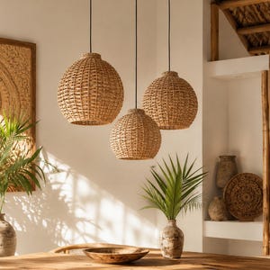 Könnte beinhalten: Drei gewebte Pendelleuchten aus Rattan in verschiedenen Größen hängen über einem Esstisch aus Holz. Die Leuchten sind an schwarzen Kabeln aufgehängt. Der Tisch ist von gewebten Stühlen umgeben, was eine warme, natürliche Ästhetik schafft.