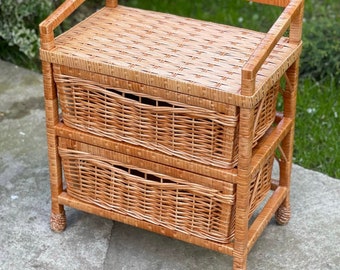 May include: A two-tiered wicker storage shelf with a natural brown finish. The shelf has two drawers and a top shelf. The shelf is made of woven wicker and has a rustic look.