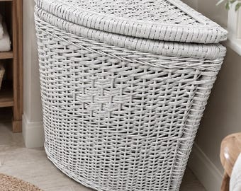 May include: A white corner laundry hamper constructed from woven wicker material. The hamper features a triangular shape designed to fit into a corner, a flat lid that sits on top, and a textured, woven exterior finish throughout the entire body.