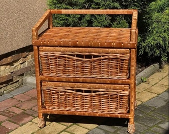 May include: A three-tiered wicker storage unit with a top shelf and two drawers. The unit is made of natural brown wicker and has a rustic, farmhouse style.