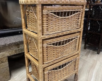 May include: A three-tiered wicker storage shelf with three drawers. The shelf is made of natural woven wicker and has a light brown color.