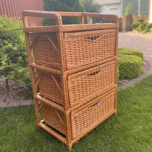 Puede incluir: Una cómoda de mimbre con tres cajones. La cómoda está hecha de mimbre natural tejido y tiene un color marrón claro.