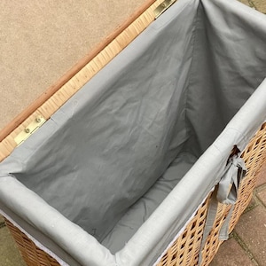 May include: A wicker storage basket with a gray fabric liner and white lace trim. The lid is open and the basket is empty.