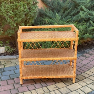 May include: A three-tiered wicker shelf unit with a natural brown finish. The shelf has a woven design and is made of natural materials.
