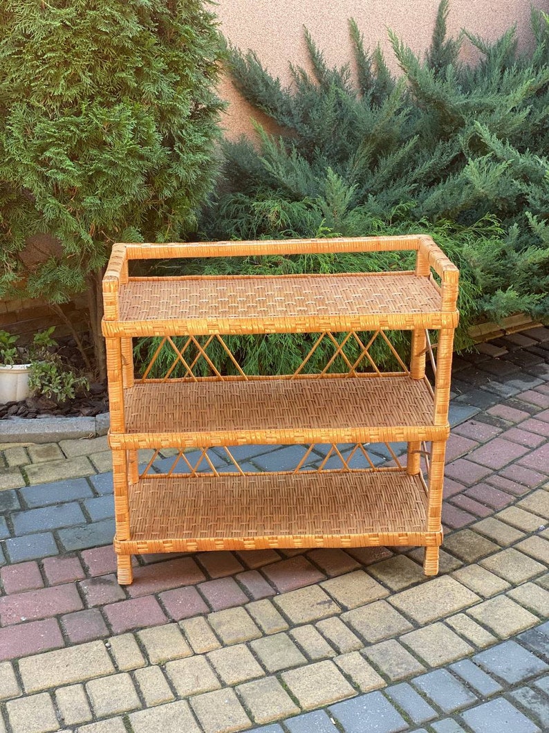 May include: A three-tiered wicker shelf unit with a natural brown finish. The shelf has a woven design and is made of natural materials.