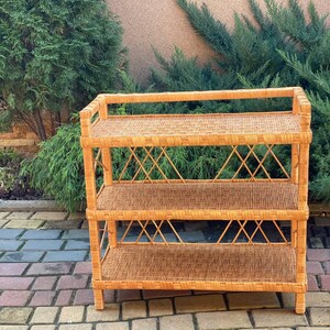 May include: A three-tiered wicker shelf unit with a natural brown finish. The shelf is made of woven rattan and has a simple, rustic design.