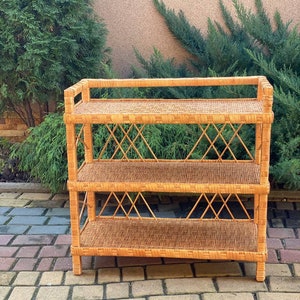 May include: A three-tiered wicker shelf unit with a natural brown finish. The shelf has a woven design and is made of natural materials.