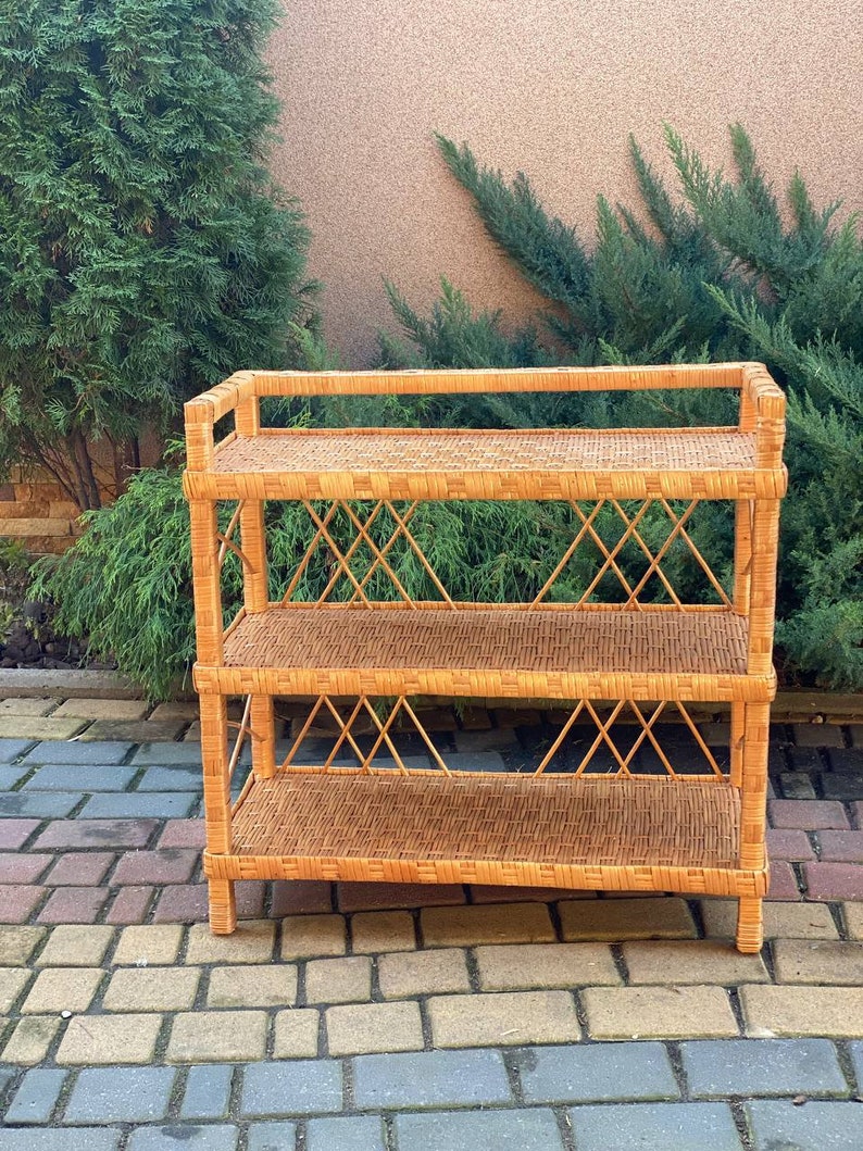 May include: A three-tiered wicker shelf unit with a natural brown finish. The shelf has a woven design and is made of natural materials.