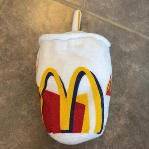 Könnte beinhalten: Weißes Plüschtier in Form eines McDonald's-Bechers mit einem roten und gelben 'M'-Logo und einem Strohhalm.