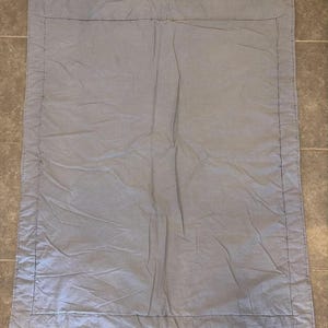 May include: A rectangular light gray quilt featuring a solid color design with a stitched border frame. The fabric has a soft, slightly wrinkled texture throughout the surface, with visible stitching lines defining the central panel and edges.