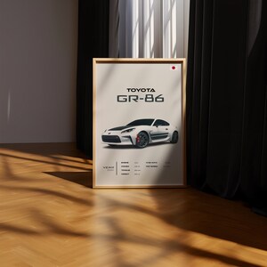 May include: A poster with a white Toyota GR-86 sports car on a white background. The poster has the text "TOYOTA GR-86" in black text at the top. The poster also includes the year, engine, power, torque, and top speed of the car.