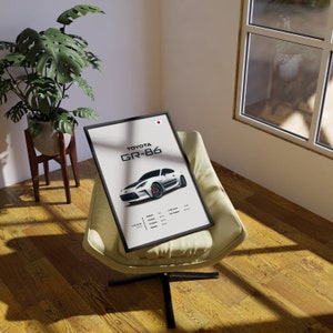May include: A black framed poster with a white Toyota GR-86 sports car on a white background. The poster has the text "TOYOTA GR-86" in black and white text. The poster also has the text "YEAR 2021" in black text.