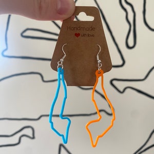 May include: A pair of handmade earrings featuring the outline of a state or region. One earring is blue and the other is orange. The earrings are hanging from a brown card with the text "Handmade with love".