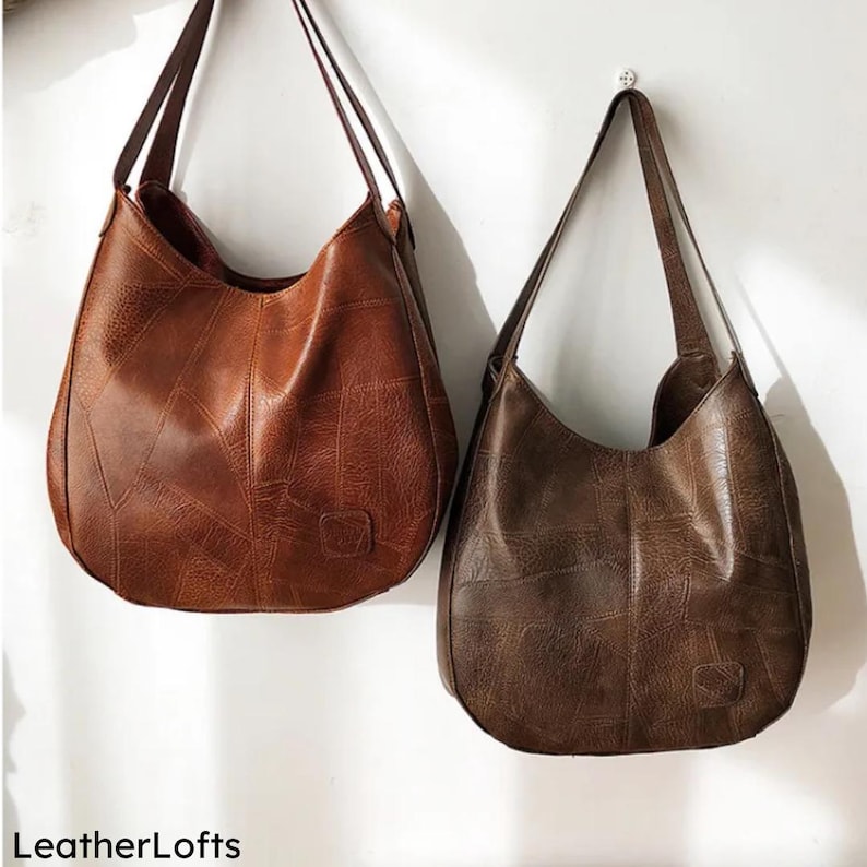 May include: Two brown leather shoulder bags with long straps hang against a white wall. The bags have a patchwork design and a small square emblem. The bags are different shades of brown, one lighter and one darker.